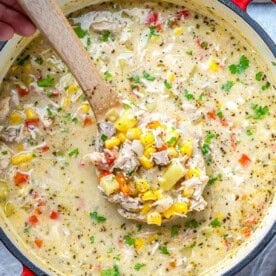 A spoonful of chicken corn chowder in a pot.