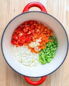 chopped onion, chopped red pepper, chopped onion and celery, and minced garlic added to a cooking pot.