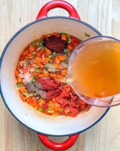 broth being added to a pot with seared veggies for soup.