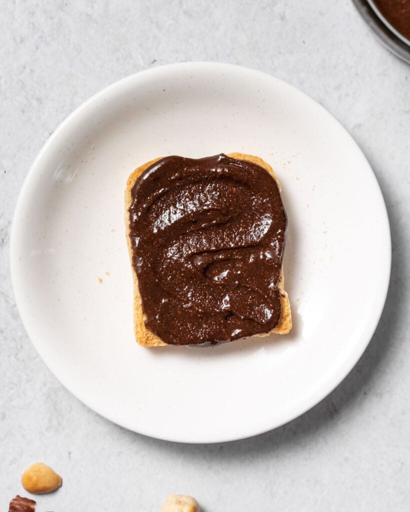 top view of a toast with Nutella over it on a round white plate 