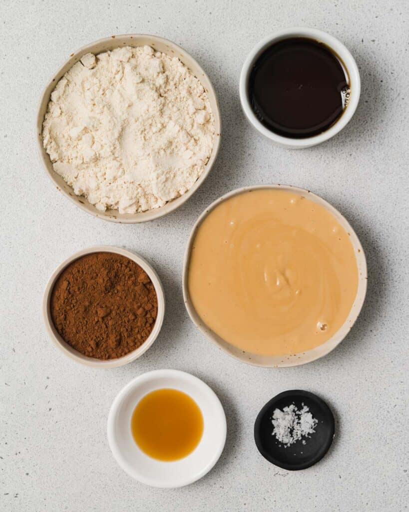 Almond flour, peanut butter, vanilla, cocoa powder and maple syrup divided into small bowls.