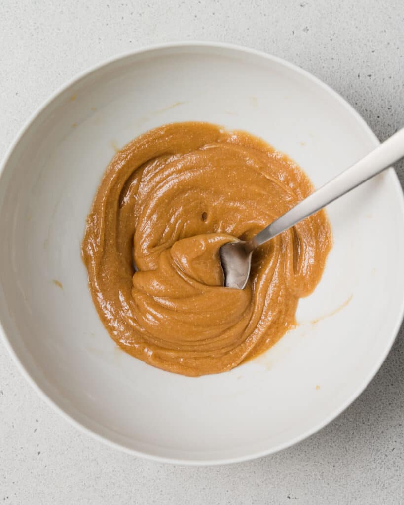 Stirring peanut butter, vanilla and maple syrup together.