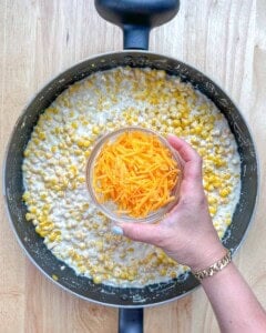 shredded cheddar cheese being added over cheesy corn.