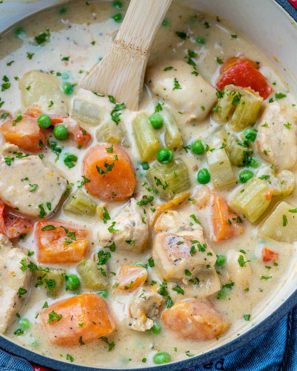 chicken stew in a pot with veggies and a spoon in the pot.