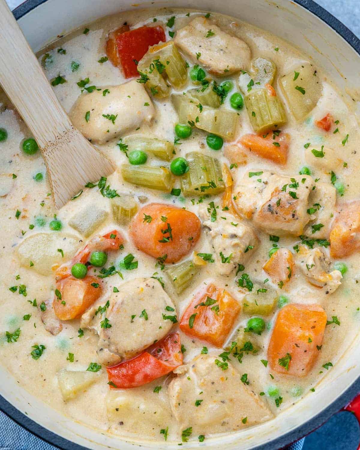 a pot filled with creamy chicken stew with a wooden spoon in the pot.