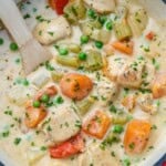 chicken stew in a pot with veggies and a wooden spoon in the pot.