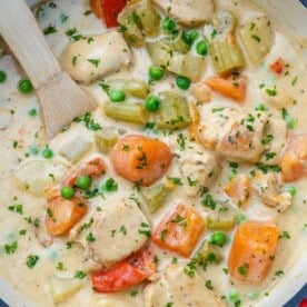 chicken stew in a pot with veggies and a wooden spoon in the pot.