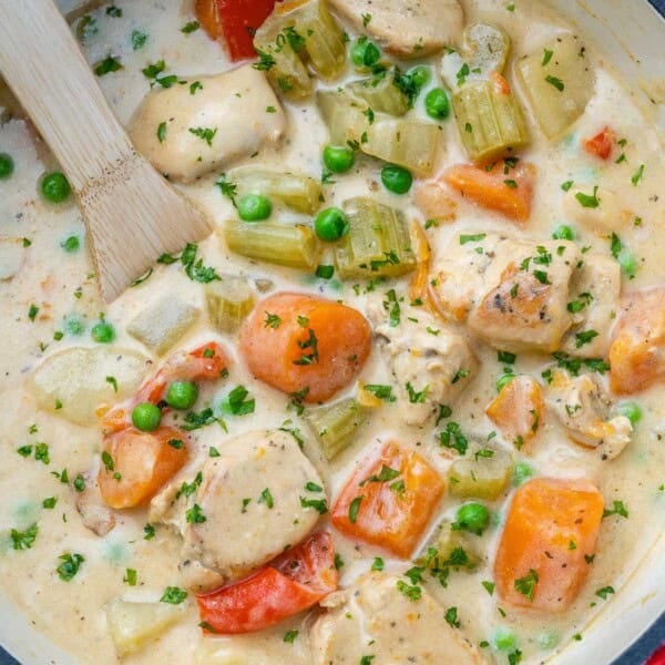 chicken stew in a pot with veggies and a wooden spoon in the pot.