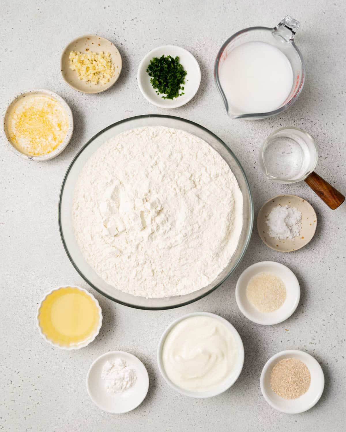 Flour, yogurt, yeast, herbs, water, milk, baking powder, sugar and salt divided into small bowls.