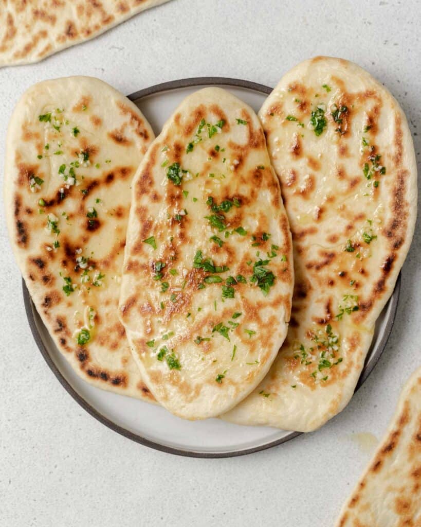 top view of 3 naan breads on a plate topped with garlic butter and chopped parsley