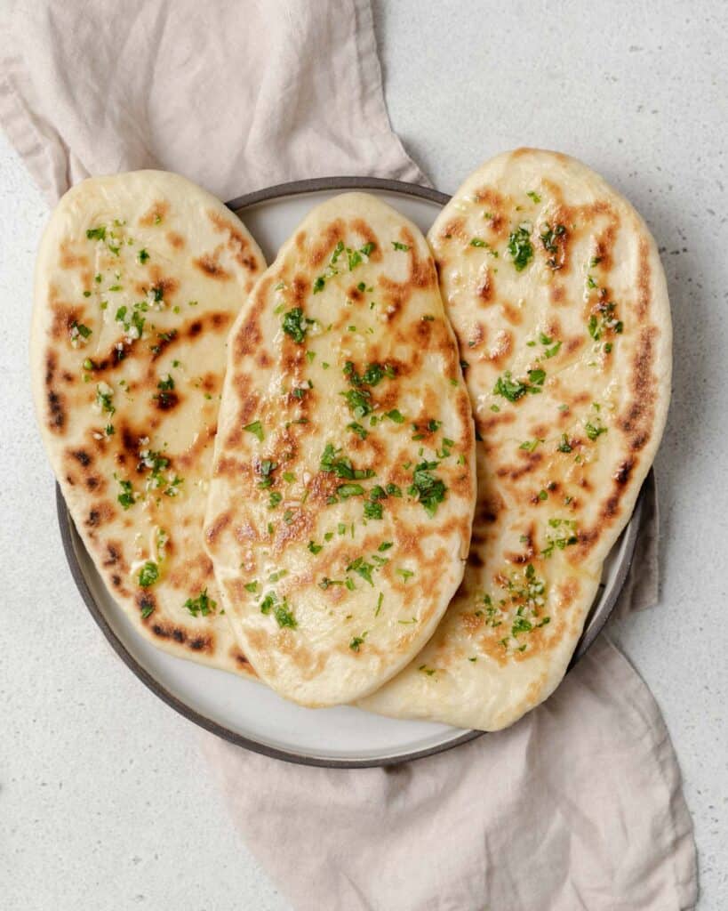 top view of 3 naan bread on a plate topped with garlic butter and chopped parsley