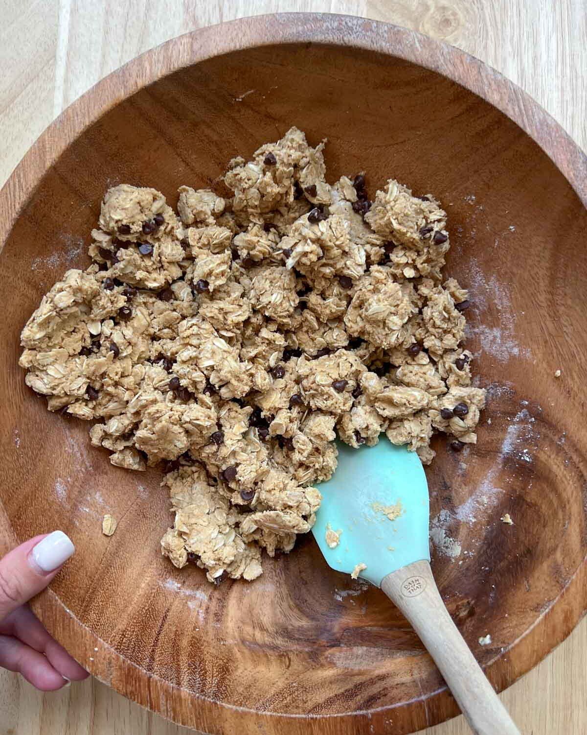 Chocolate chips mixed in with the peanut butter oats dough in a wooden bowl.