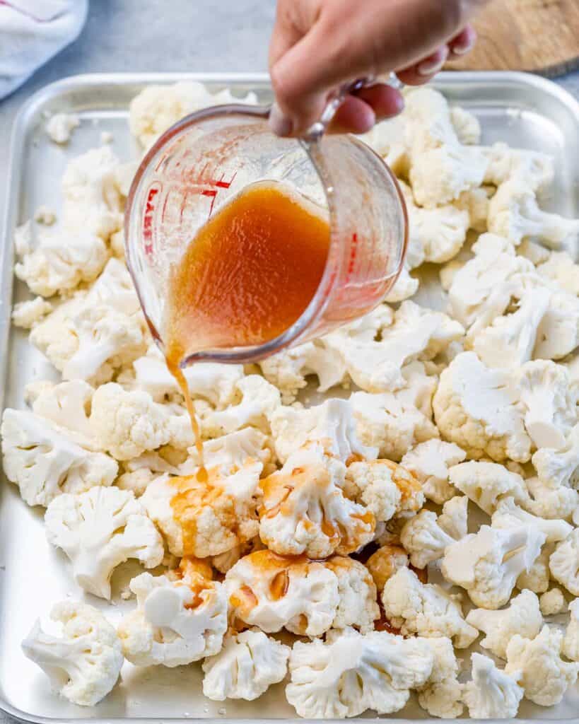 hand holding a jar with sriracha and honey mix pouring over cauliflower pieces