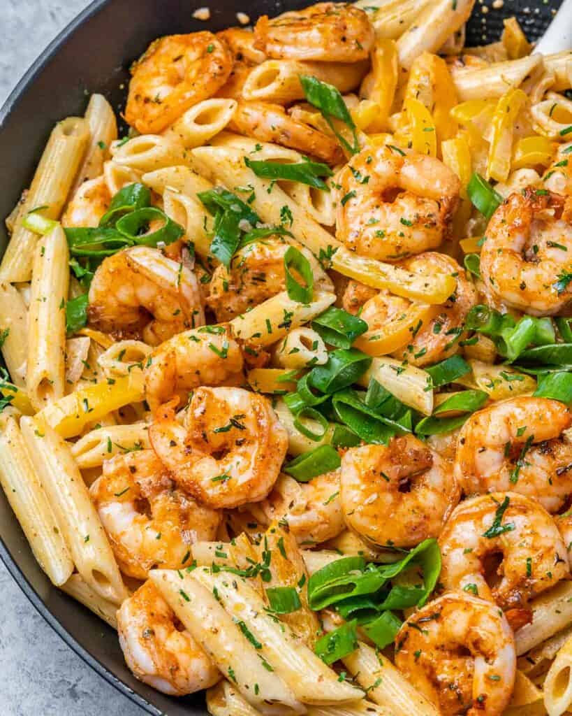 top close up view orange seasoned pasta with shrimp topped with sliced green onions