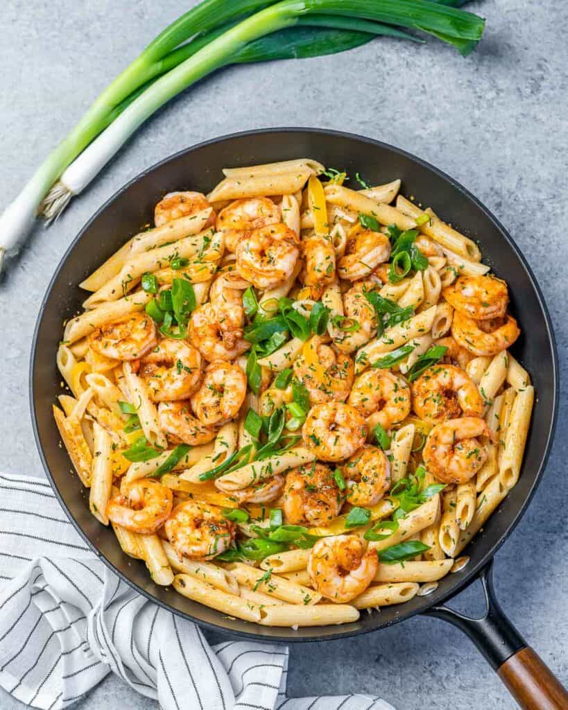 top view of a black skillet with shrimp and pasta that is creamy based and orange-looking with a green onion sprig next to the skillet