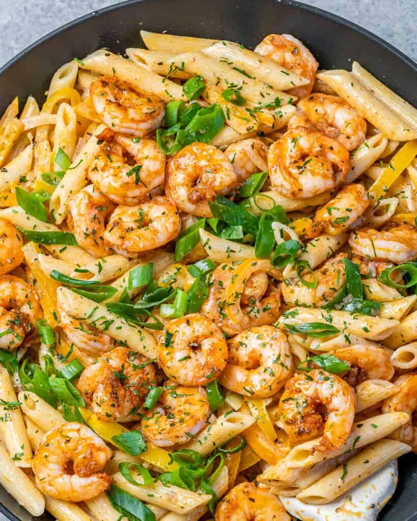top close up view of shrimp and penne pasta in a black skillet that is garnished with sliced green onions