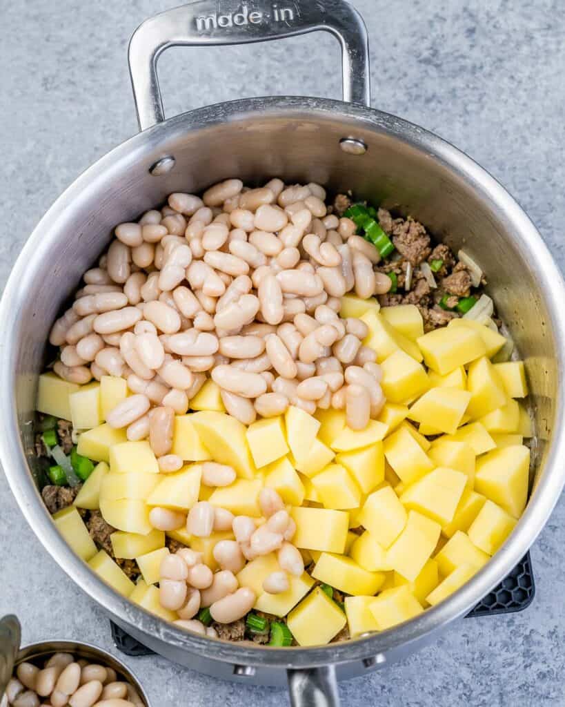 Adding beans and potatoes to a soup pot.