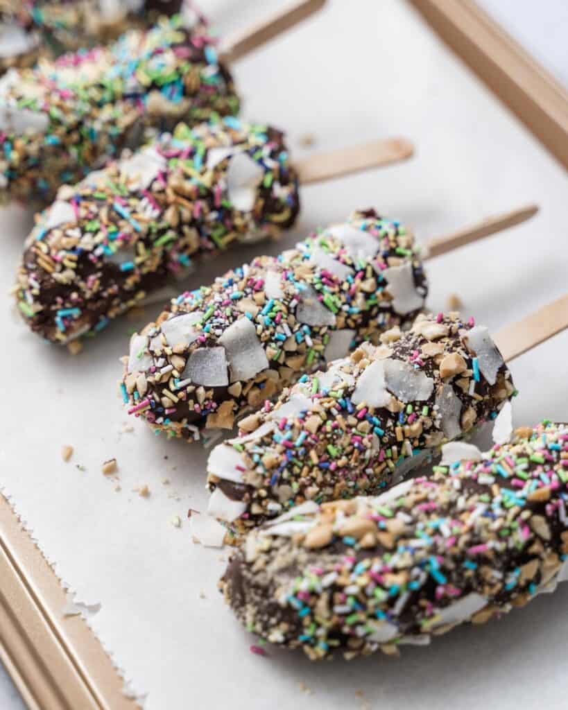coated banana pops in sprinkles on a parchment 