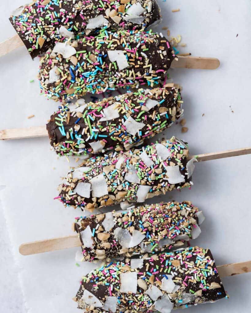 6 banana pops covered in sprinkles laid out on a flat surface 
