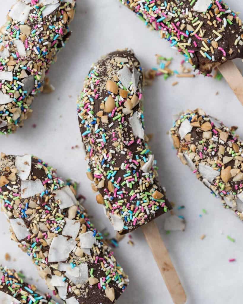 banana pop coated in sprinkles laid out on a flat parchment paper 