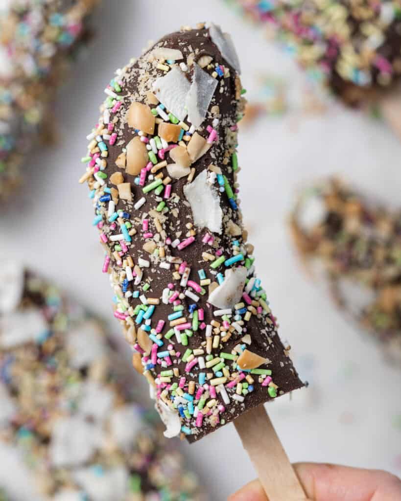 hand holding a single banana pop covered in sprinkles