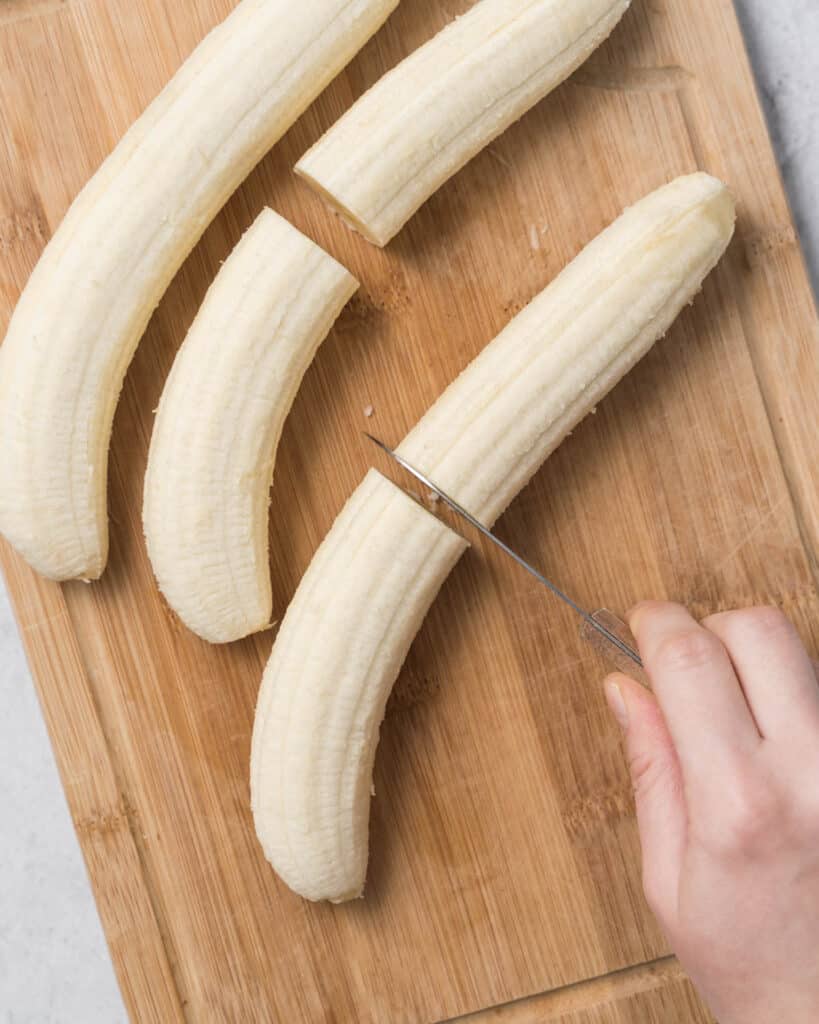 hand cutting peeled banana in half on a cutting board