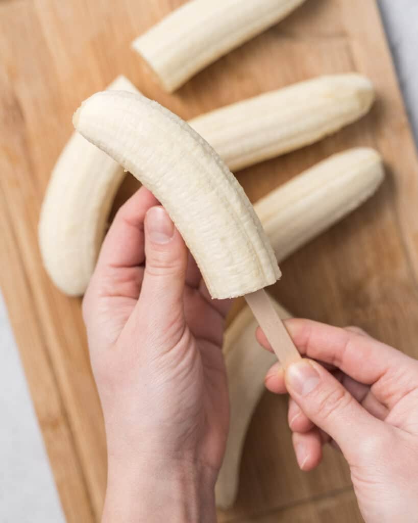 hand inserting a popsicle stick into banana 