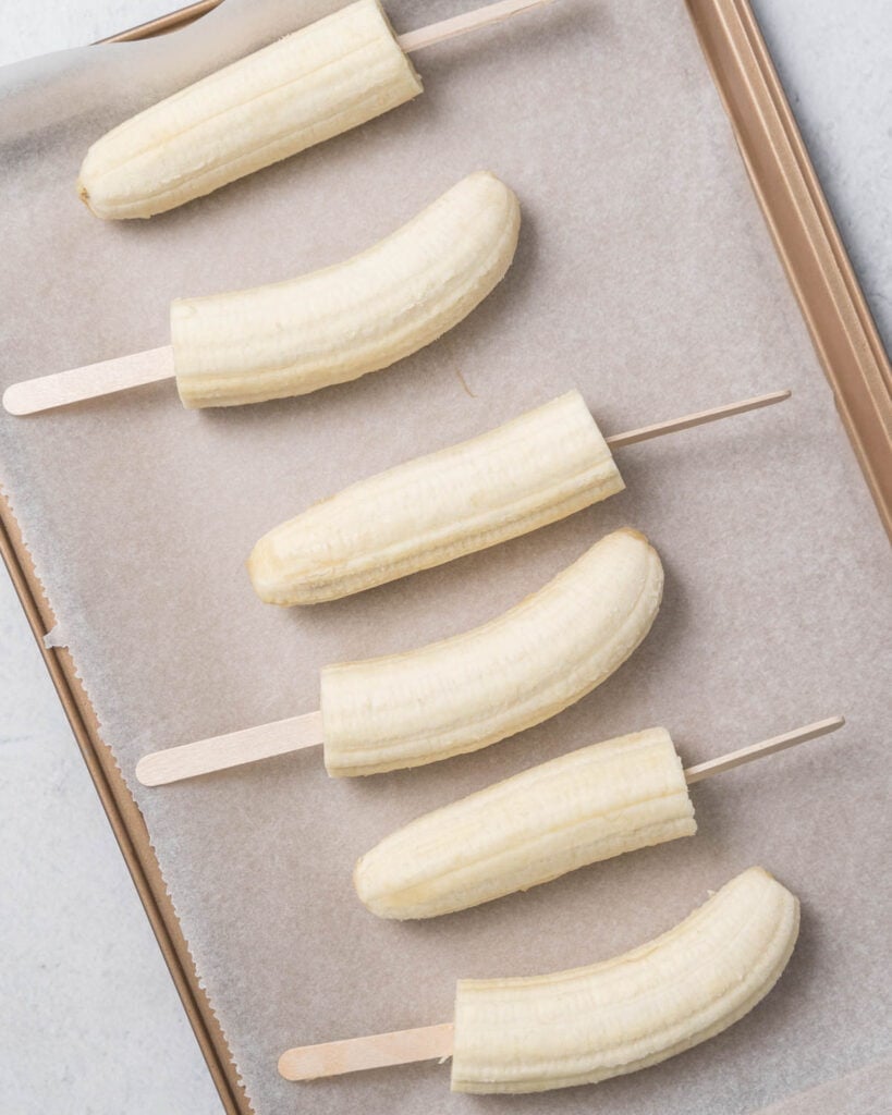 banana pops added over parchment paper on a pan to be frozen
