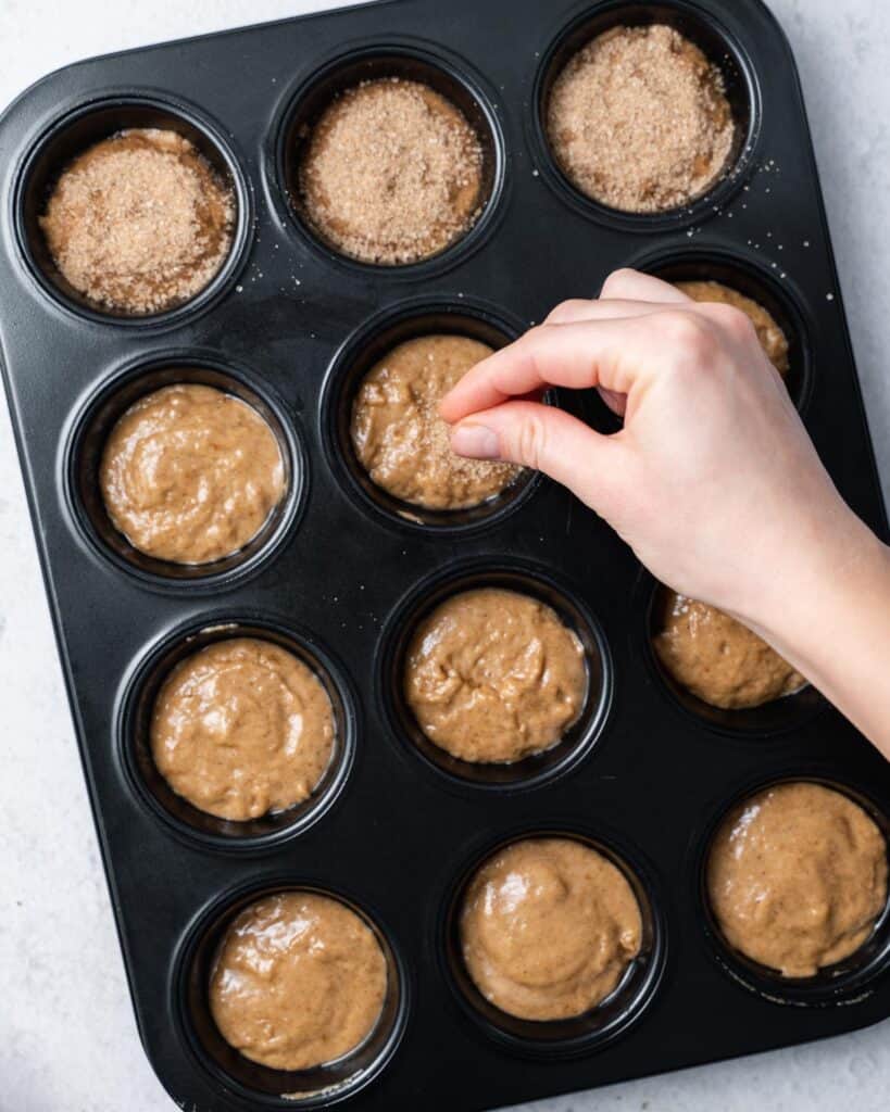 Sprinkling cinnamon and sugar over the tops of muffin batter in a pan.