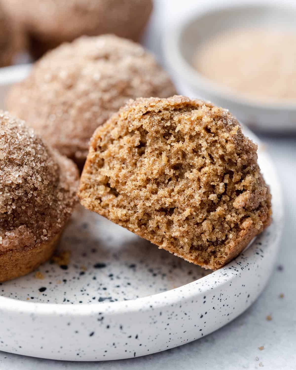 Muffin with a cinnamon sugar topping cut in half on a white plate.