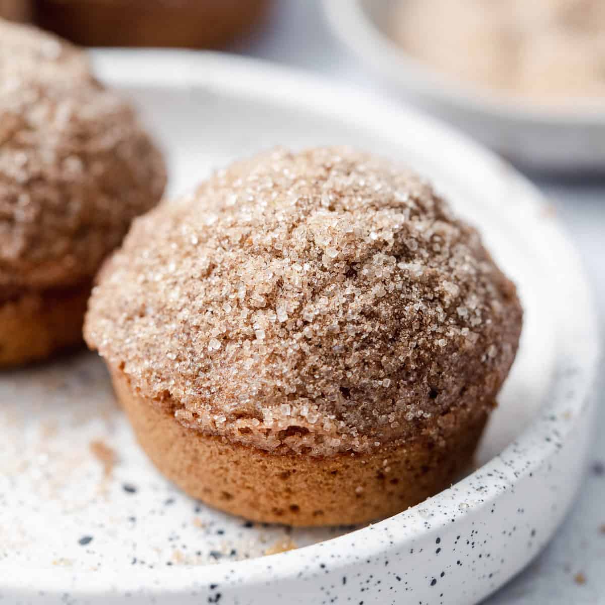 side shot of a single muffin topped with cinnamon sugar on a white plate