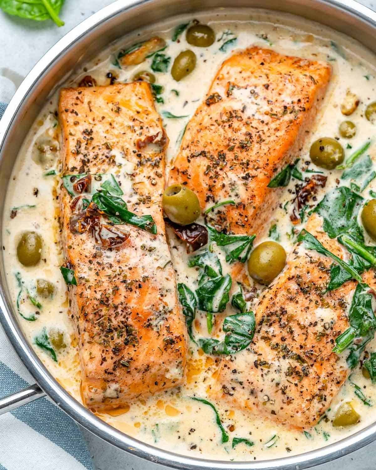 cooked salmon in a creamy tuscan spinach sauce in a skillet.