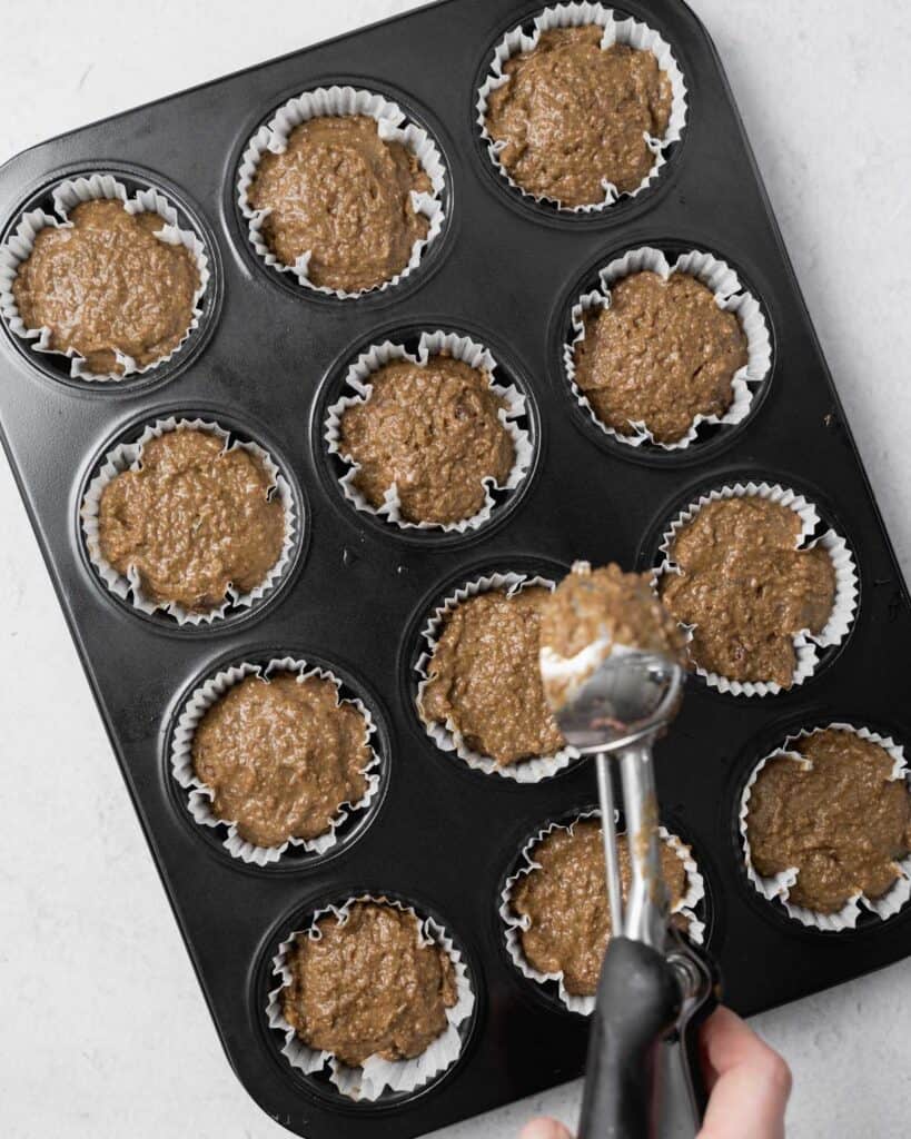 Using an ice cream scoop to add batter to a muffin pan.