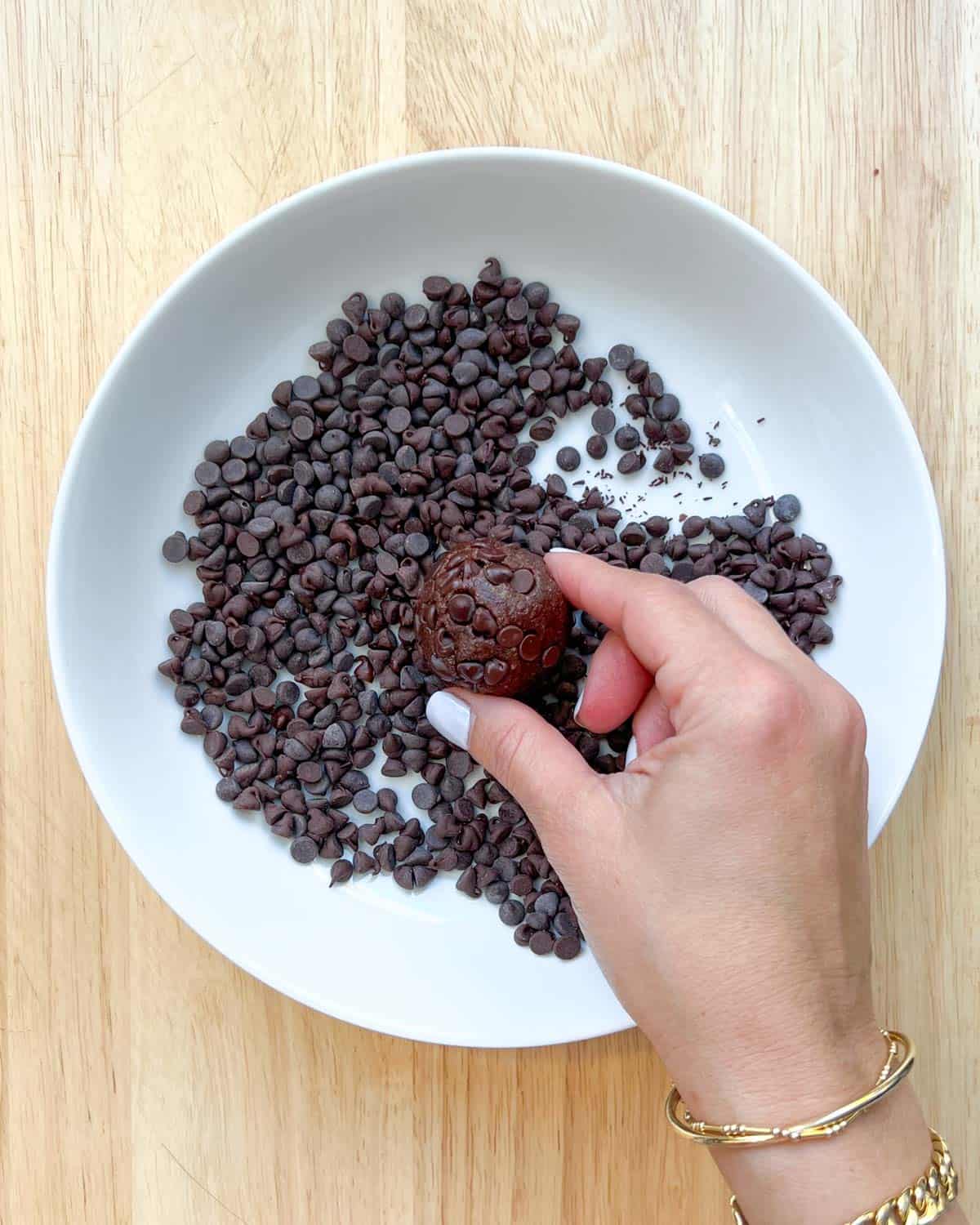 Hand-holding brownie bites over chocolate chips in a dish to roll it on the chocolate chip to coat it.