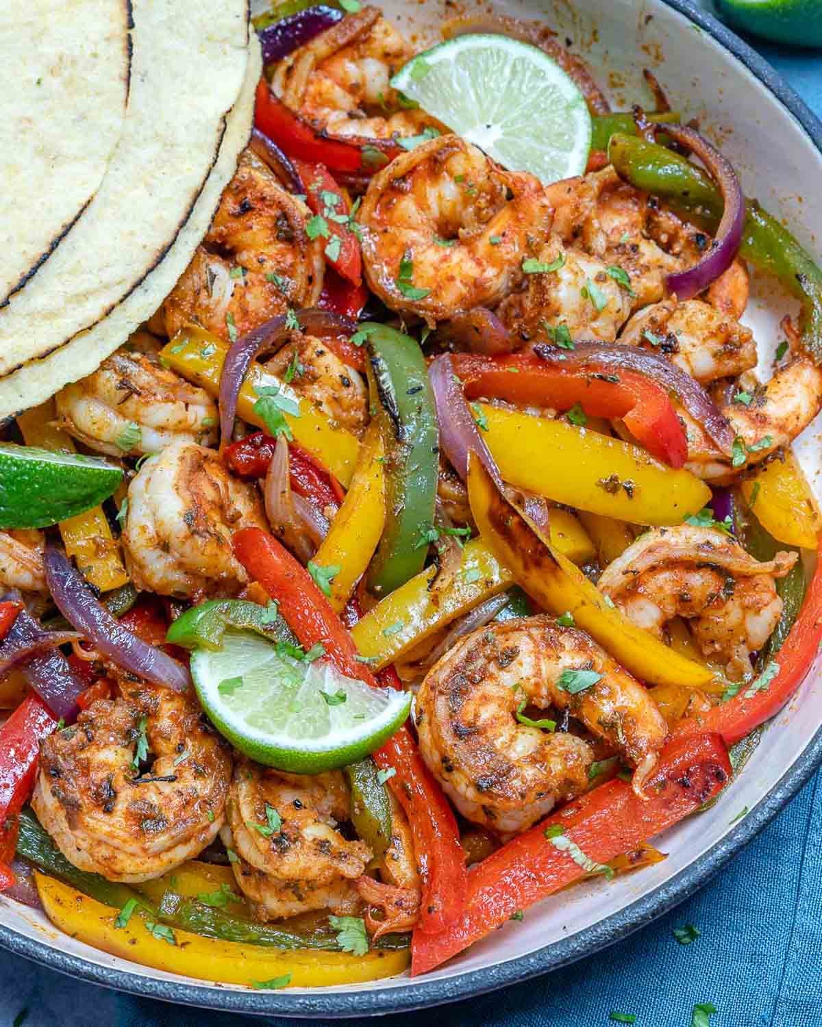 shrimp fajitas in a skillet with seared veggies and tortilla.