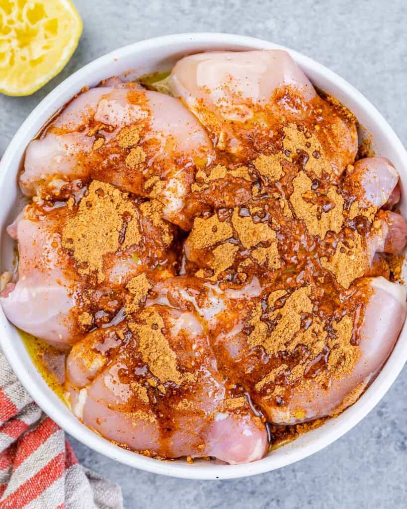 Adding taco seasoning to raw chicken thighs in a bowl.