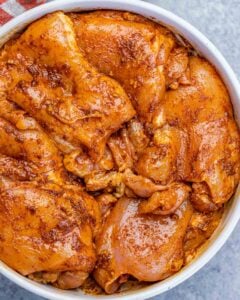 Chicken thighs marinating in a white bowl.