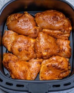 Seasoned chicken thighs cooking in an air fryer.