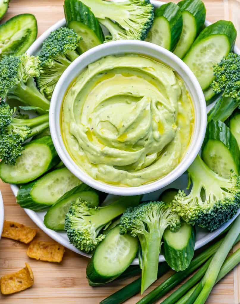 top view of green veggie platter with a bowl of green avocado dip