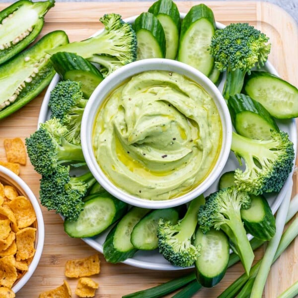 top view green dip made with avocado and yogurt surrounded by slices of cucumbers and broccoli