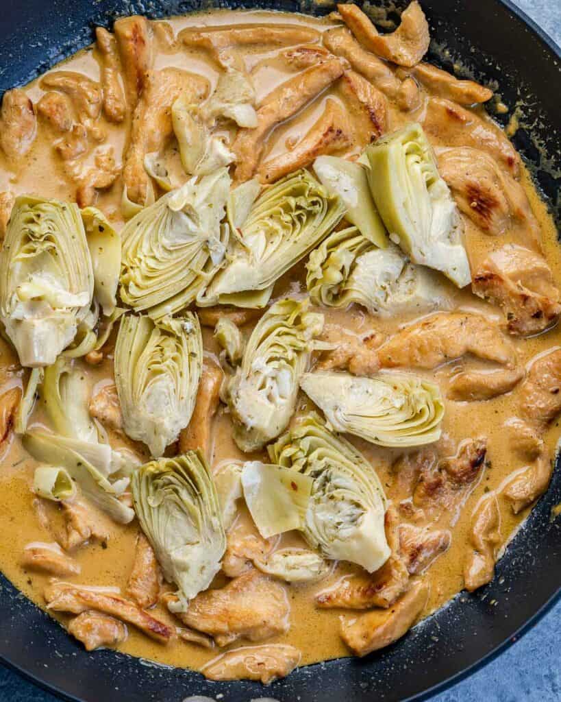 artichoke added over the creamy chicken sauce on a black skillet