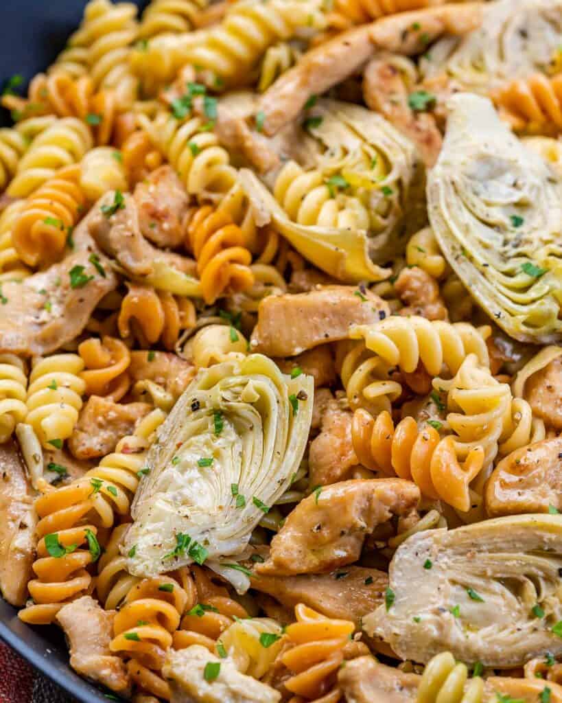 close up image of multi-colored pasta in a pan with artichoke and chicken 