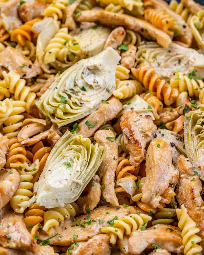 close up multi-colored pasta in a dish artichoke and chicken slices 