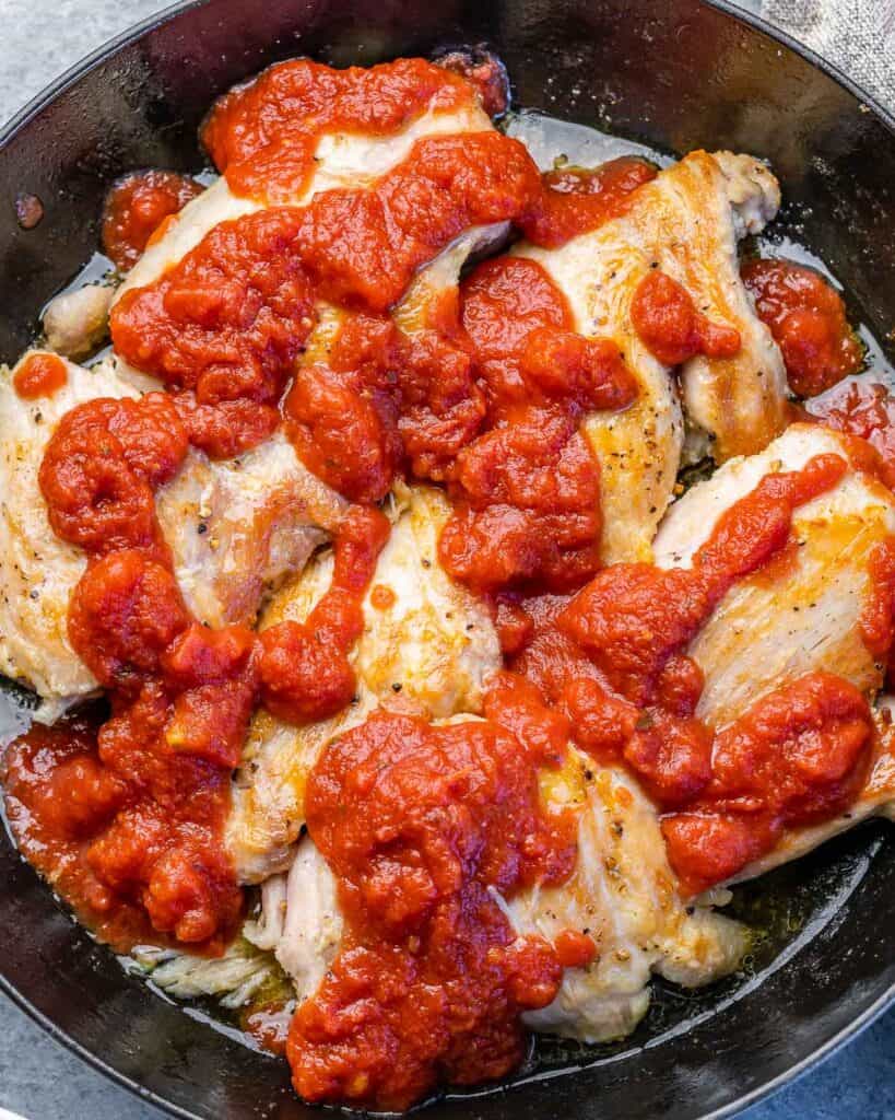 Chicken thighs covered in a red sauce cooking in a pan.