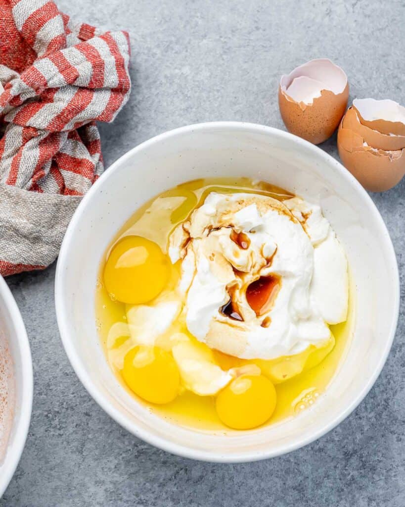 yogurt eggs and vanilla added in a white bowl to be mixed for waffle batter 