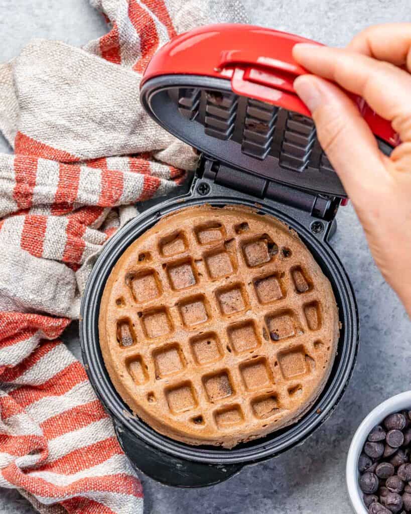 hand opening the waffle maker with freshly made chocolate waffles in it still