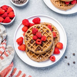 top view of chocolate waffles on a plate topped with fresh raspberries and chocolate chops