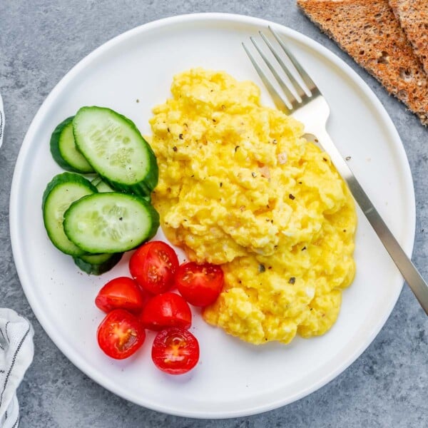 top view of scrambled cottage cheese eggs with chopped cherry tomatoes and sliced cucumber on the left of the scrambled eggs