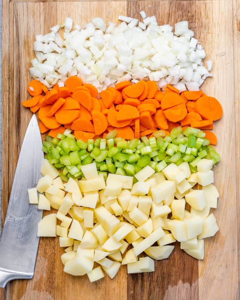 Chopped carrots, celery, onion and potatoes on a cutting board.