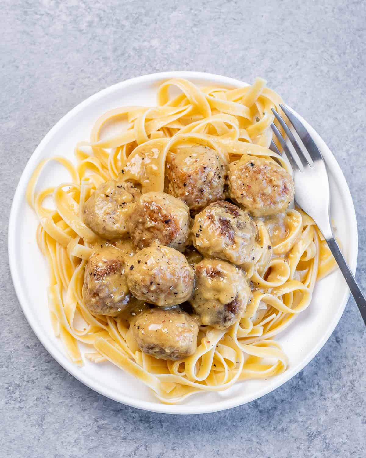 Swedish meatballs served over pasta on a white plate.